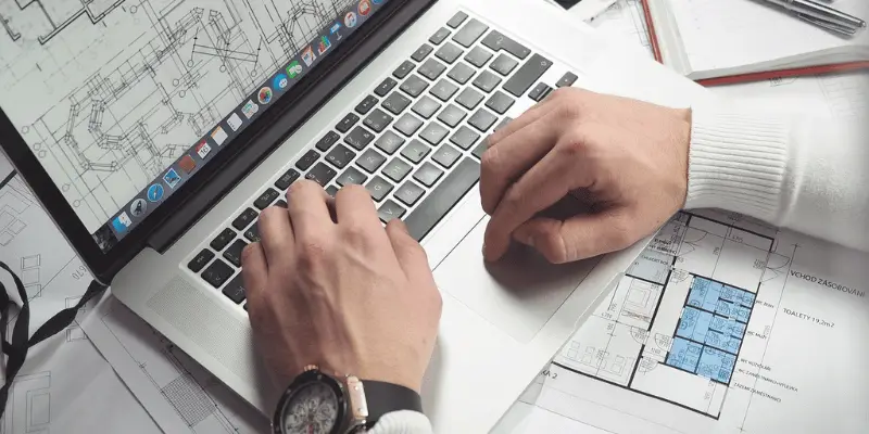 Man with watch and glasses analyzes floor plan on Macbook Pro
