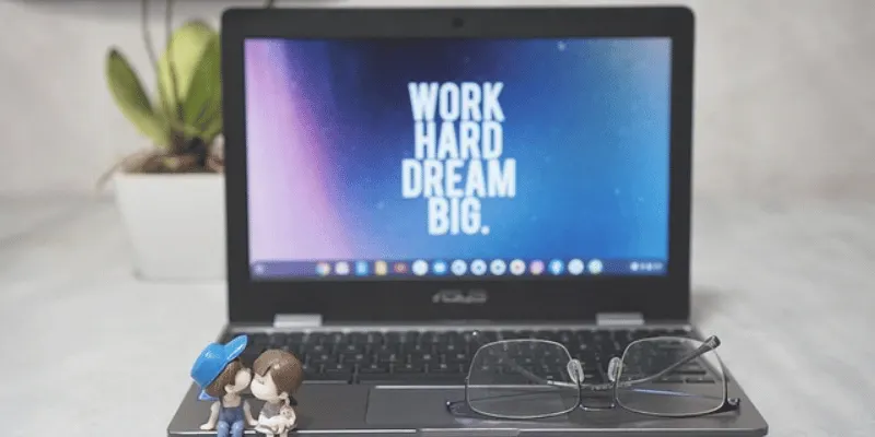 Asus Chromebook with "Work Hard, Dream Big" quote, glasses, and decorative figurines
