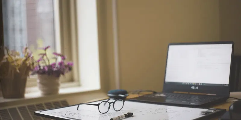 Laptop, glasses, and notebook on a table with plants
