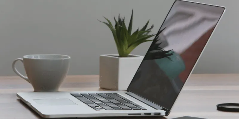 A small workspace with a laptop, coffee, and a plant.
