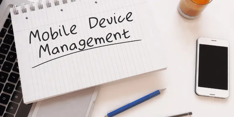 Notebook with handwritten Mobile Device Management on a desk with a smartphone Notebook with handwritten Mobile Device Management on a desk with a smartphone