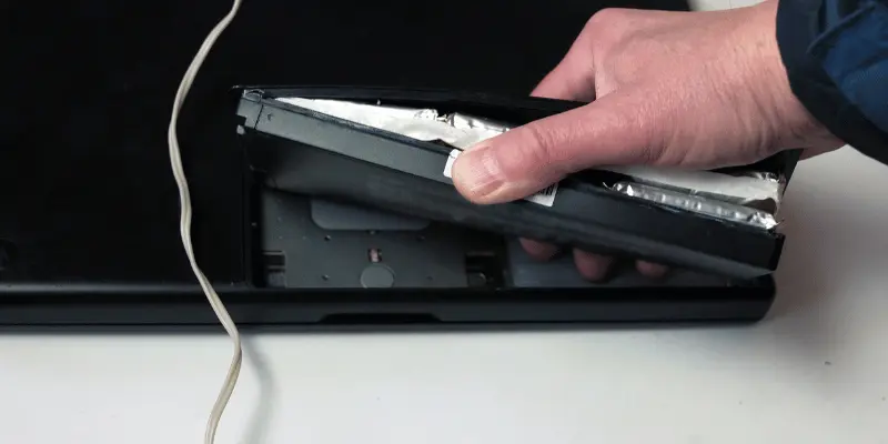 Hand taking out a bulging laptop battery, highlighting the risks of battery swelling.