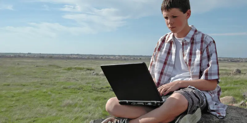 Boy sitting on a rock with laptop, enjoying nature and technology