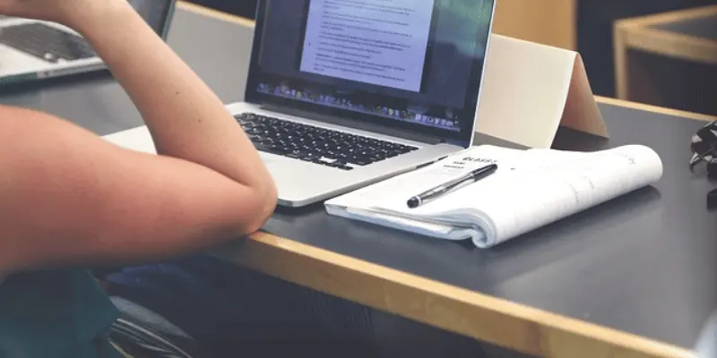 Person working on a laptop with notes in a classroom