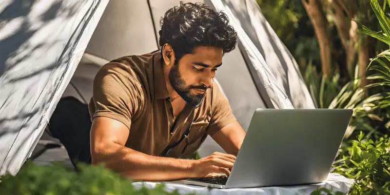 A person using a laptop in a cozy outdoor tent setup with lush greenery around