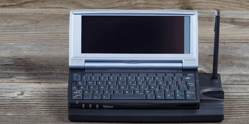 Classic gray laptop computer with black keyboard and antenna displayed on wooden surface background